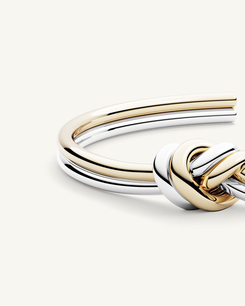 A polished stainless steel bangle in 14k gold from Waldor & Co. One size. The model is Dual Knot Bangle.
