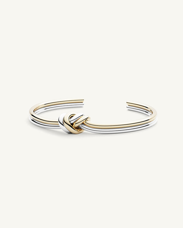 A polished stainless steel bangle in 14k gold from Waldor & Co. One size. The model is Dual Knot Bangle.