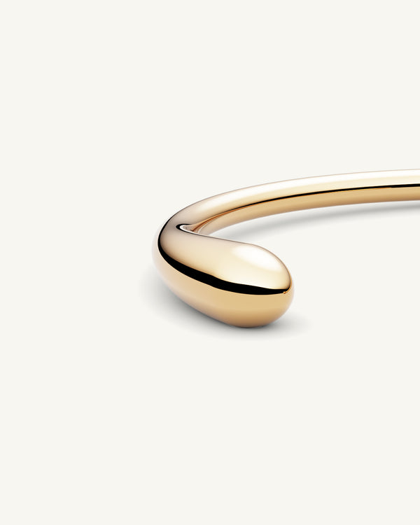 A polished stainless steel bangle in 14k gold from Waldor & Co. One size. The model is Teardrop Bangle Polished