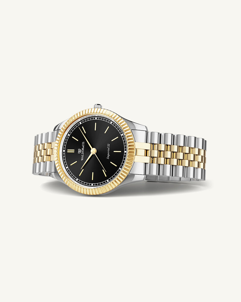 A round womens watch in silver and 14k gold from Waldor & Co. with black sunray dial and a second hand. Seiko movement. The model is Imperial 32 Positano 32mm.