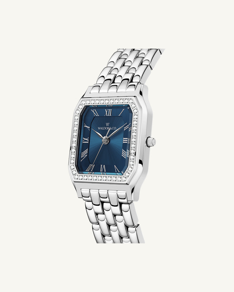 A square womens watch in Rhodium-plated 316L stainless steel from Waldor & Co. with dark blue dial. Bezel with premium crystals. Diamond Cut Sapphire Crystal glass dial. Seiko movement. The model is Eternal 22 Bellagio Pavè.